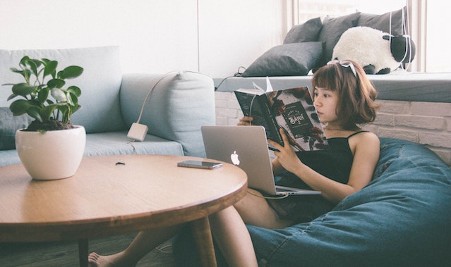 someone sitting on a bean bag reading a book with a laptop on their lap